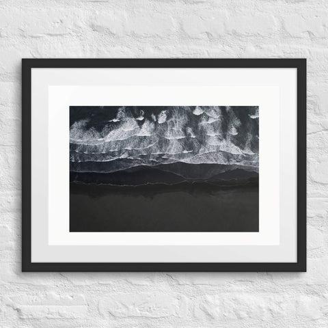 Framed poster with abstract black and white ocean wave design on a white brick wall.