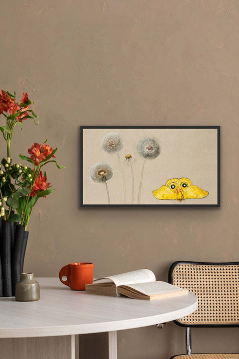 Framed poster with floral art and whimsical creature on a wall above a table setting.