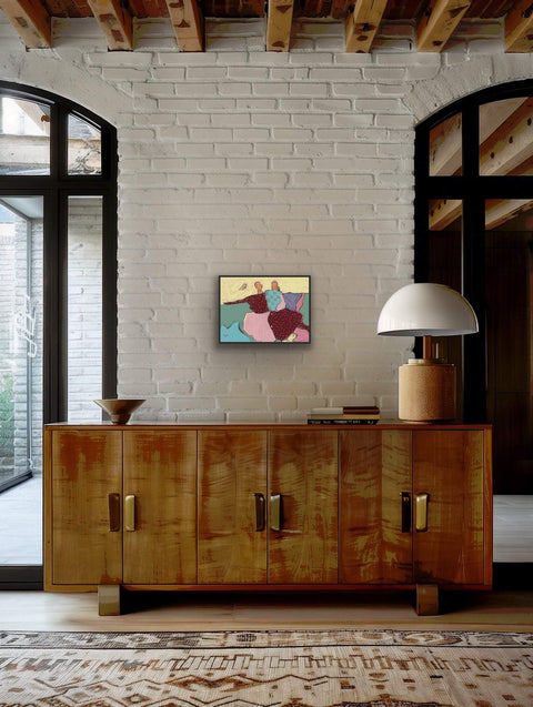 Framed "Sisters" poster by Joyce Yiu on a white brick wall above a wooden cabinet.