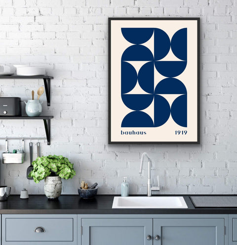 Framed poster with geometric Bauhaus design in navy blue on a brick wall above a kitchen countertop.