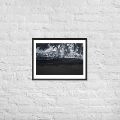 Framed poster of ocean waves meeting dark sand beach with black frame.